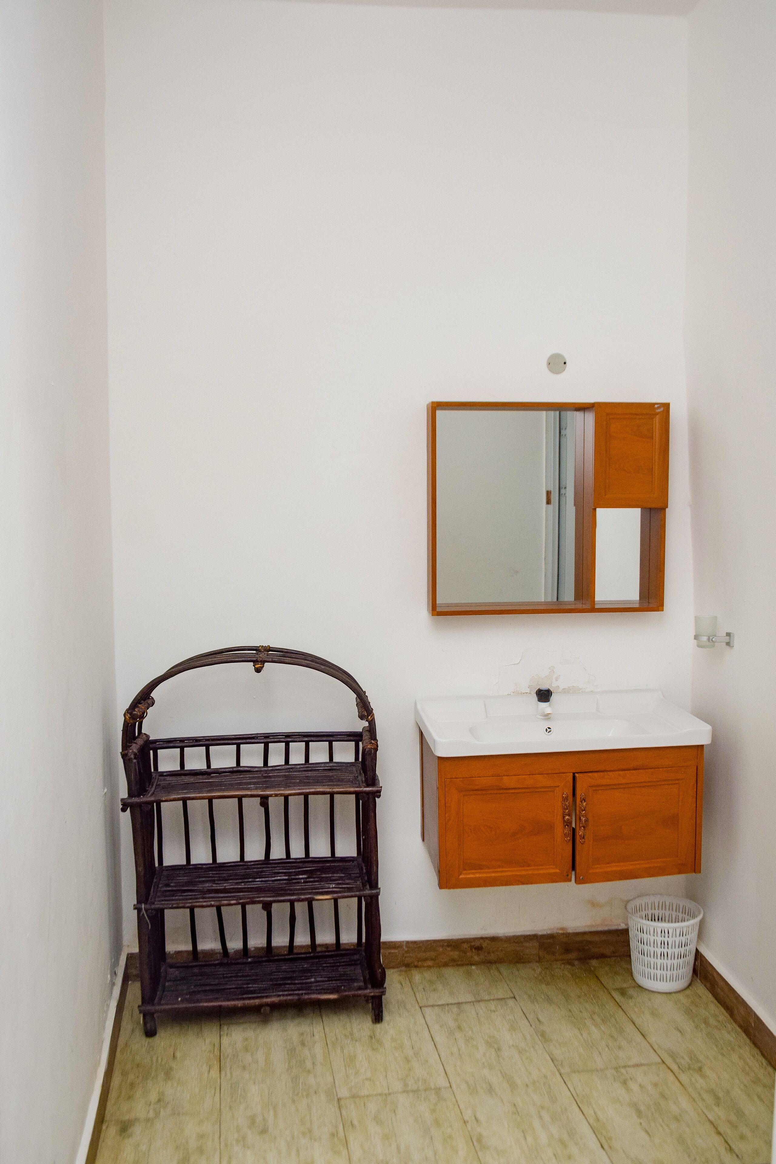 Une salle de bain avec un meuble-lavabo en bois, un miroir et une étagère en osier.