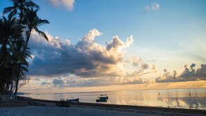 A beach with palm trees, boats, and a calm sea under a partly cloudy sky. - SHERATTON BEACH VILLAGIO HOTEL (Mombasa)