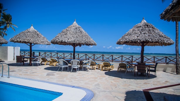 A poolside area with a clear view of the ocean, thatched umbrellas, and lounge chairs. - SHERATTON BEACH VILLAGIO HOTEL (Mombasa)