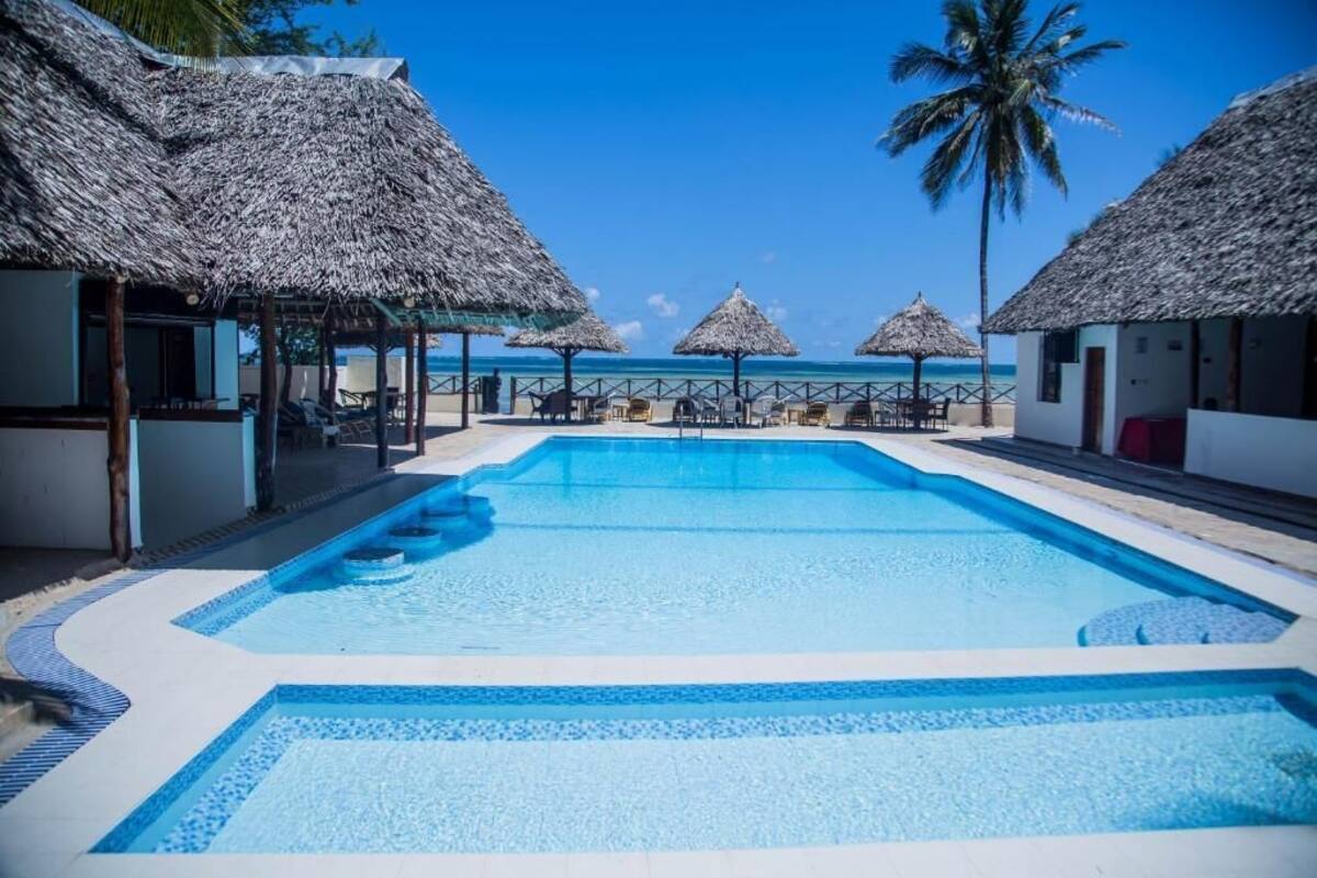 Un espace piscine agrémenté de structures à toits de chaume, d’une eau d’un bleu cristallin et offrant une vue sur l’océan.