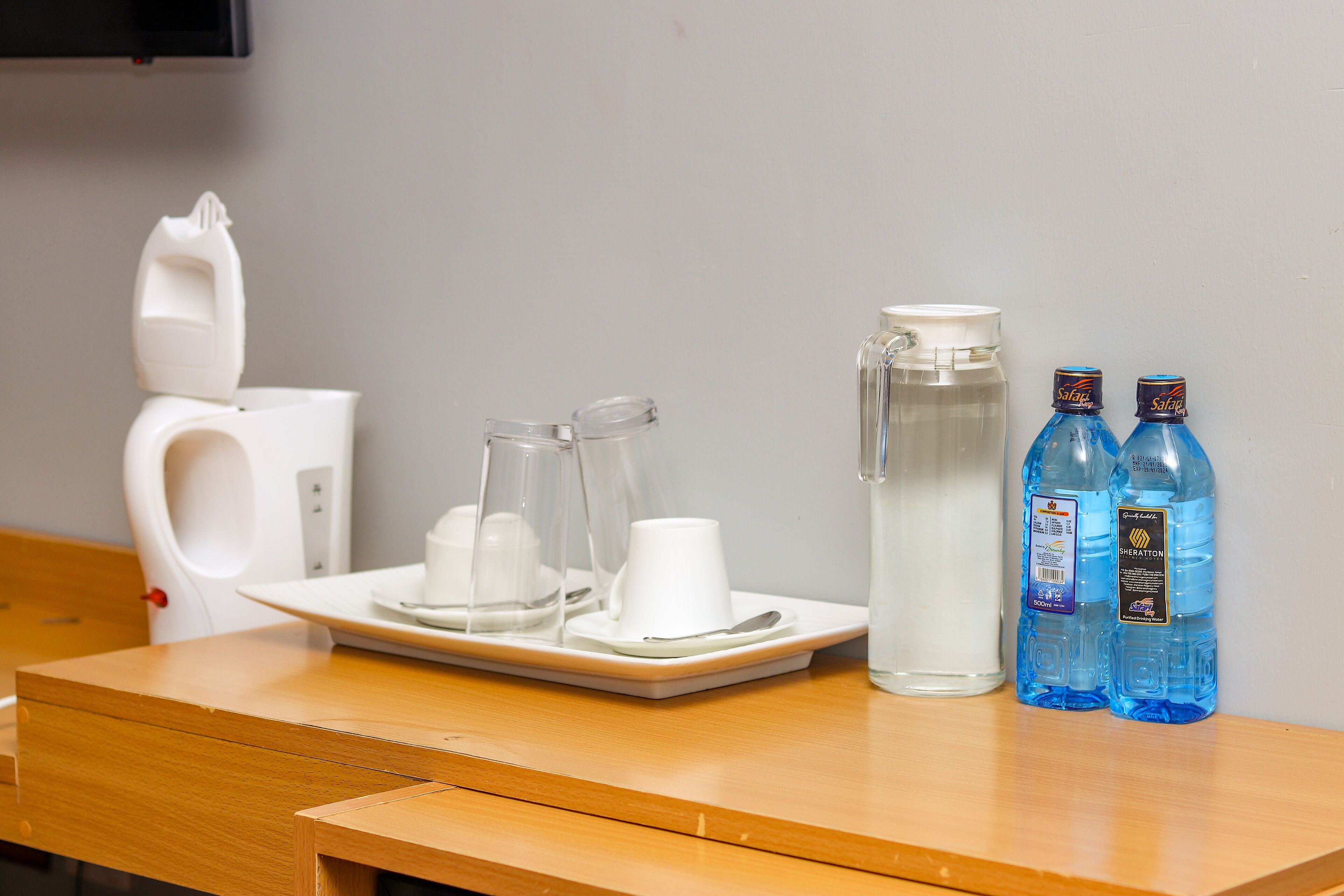 A wooden table with a water pitcher, two glass cups, and two bottles of water.