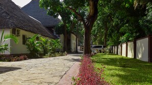 A pathway leading to a building with a thatched roof, surrounded by lush greenery and a well-maintained lawn. - SHERATTON BEACH VILLAGIO HOTEL (Mombasa)