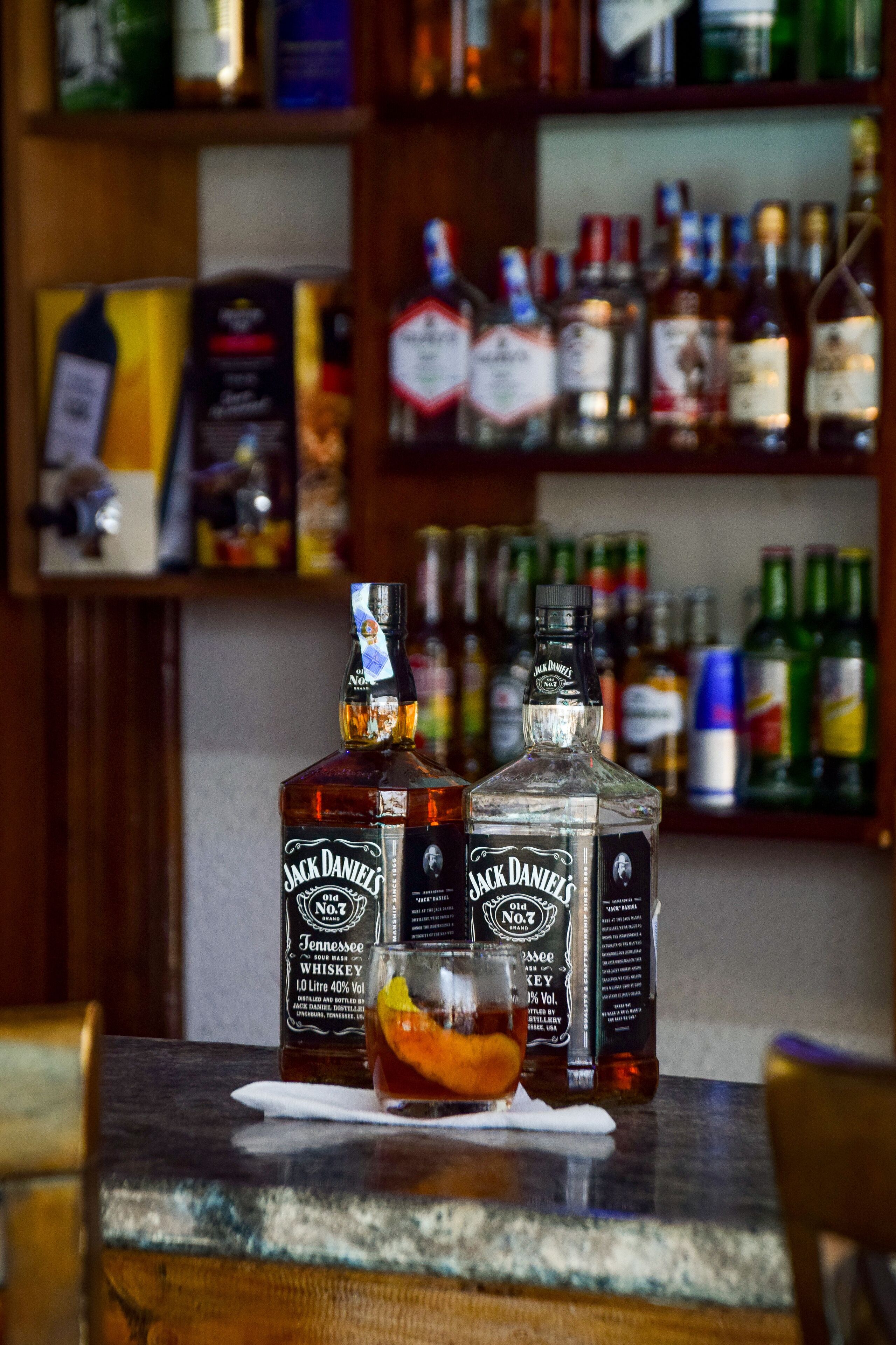 A bar setting with two Jack Daniel's bottles and a glass of whiskey on a wooden counter.