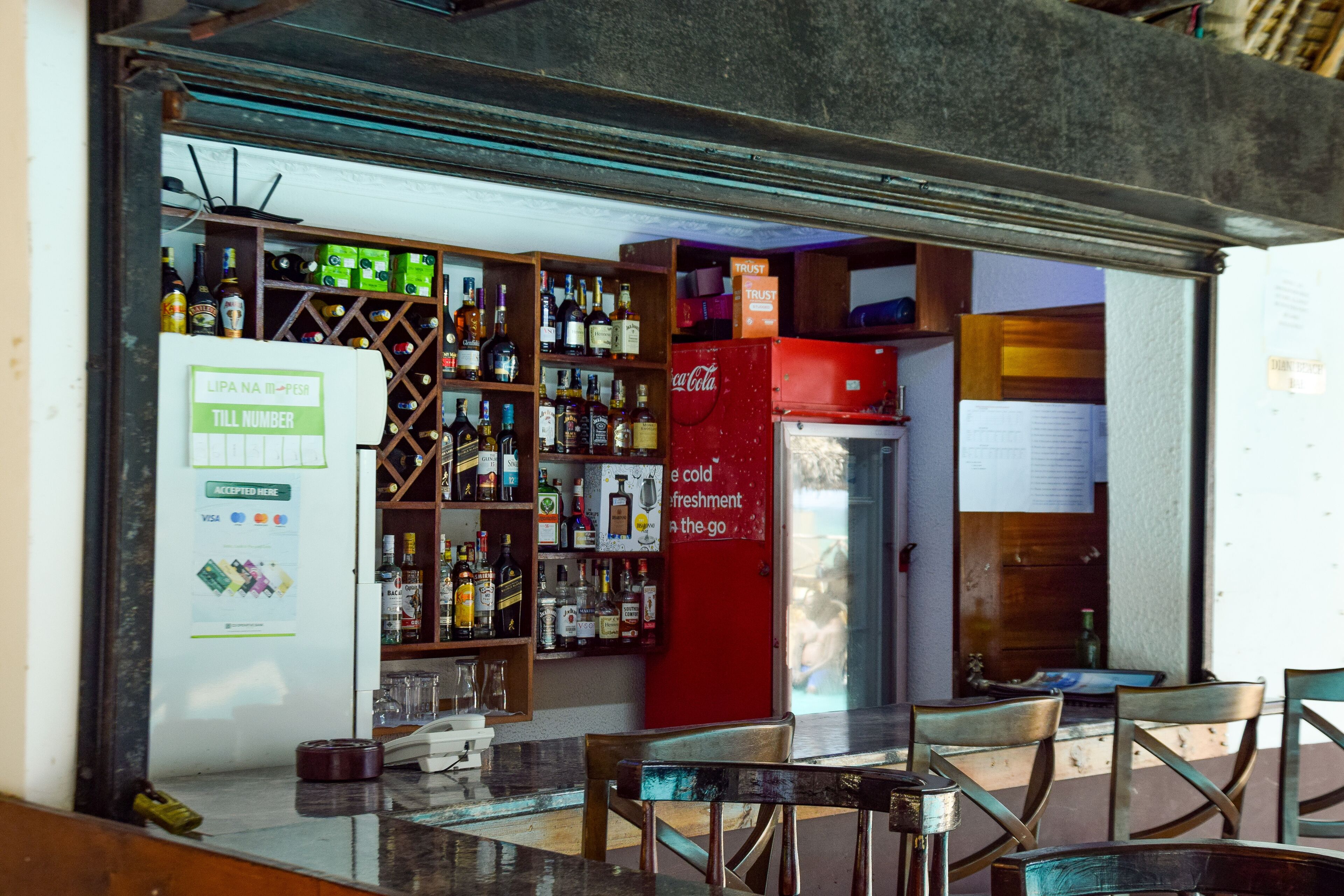 Eine Bar mit Regalen voller Spirituosenflaschen, einem Kühlschrank und einer Sitzecke mit Tischen und Stühlen.