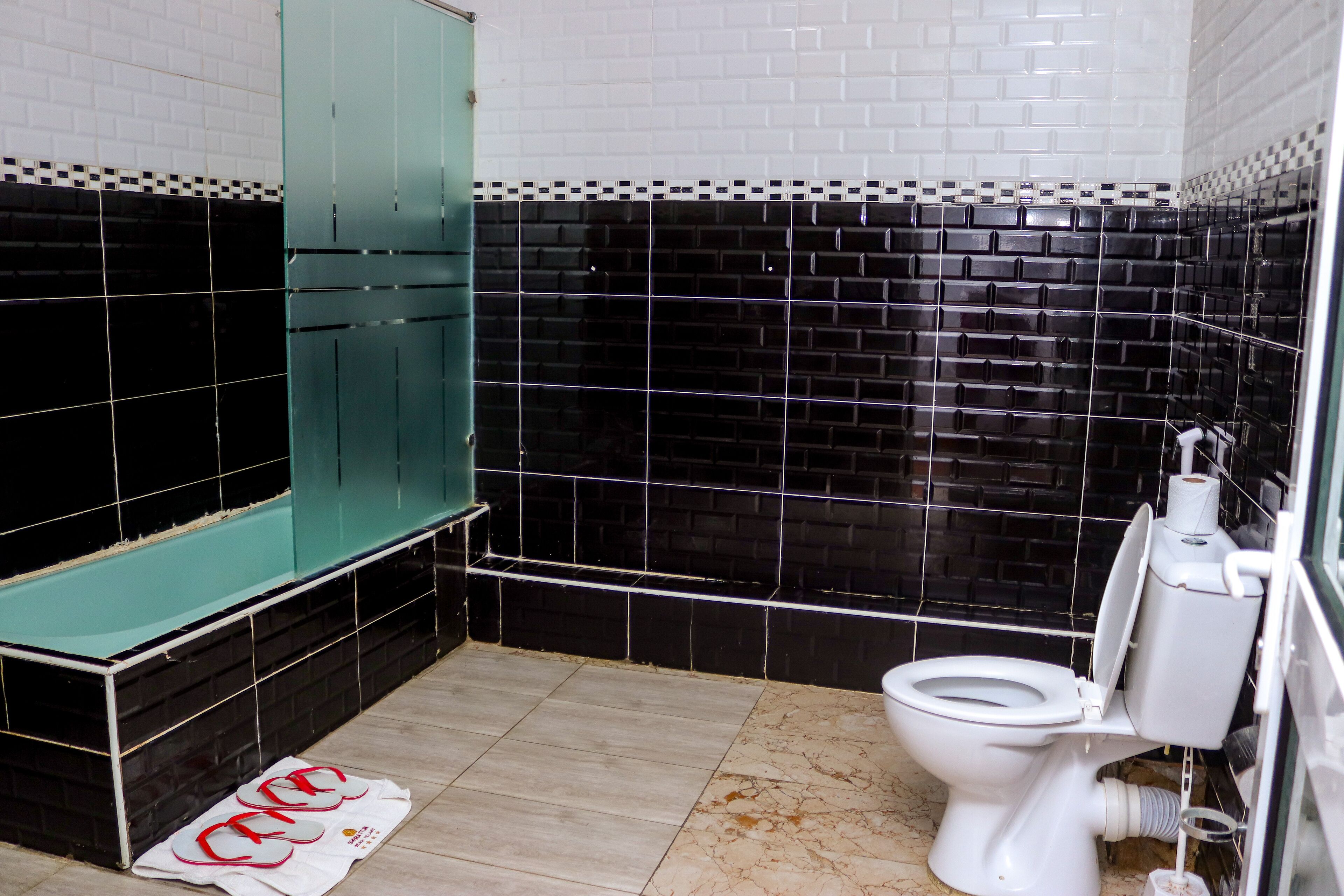 Une salle de bain avec des murs carrelés en noir et blanc, des toilettes blanches et une cabine de douche verte.