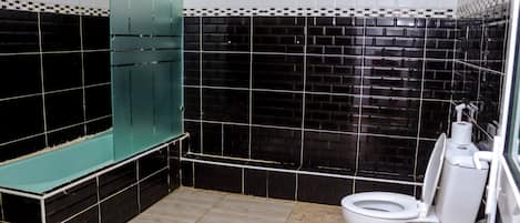 Un baño con paredes de azulejos blancos y negros, un inodoro blanco y un box de ducha verde.