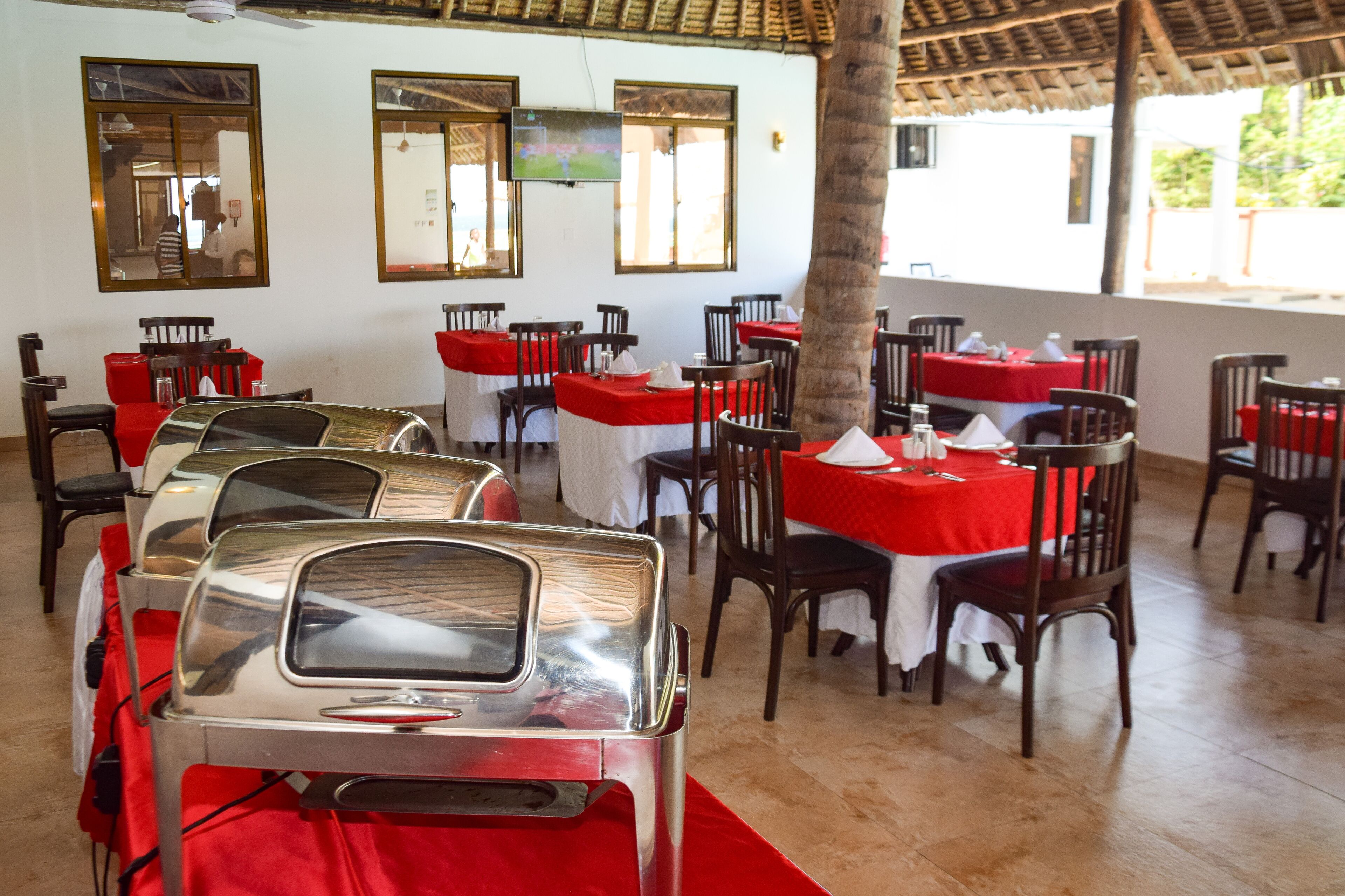 A restaurant with tables covered in red tablecloths, wooden chairs, and a TV mounted on the wall.