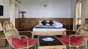 A room with a bed, two wicker chairs with red cushions, a small table, and a wall-mounted light fixture.