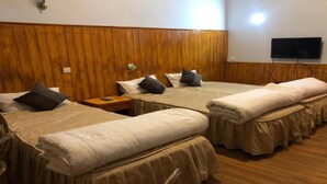 A hotel room with three beds, wooden paneling on the walls, a flat-screen TV mounted above the beds, and a wooden floor.