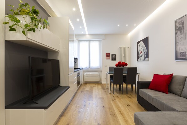 A modern living room with a flat-screen TV, a dining area with a table and chairs, and a sofa with red cushions. - notaMI - House San Cristoforo M4 (Milan)