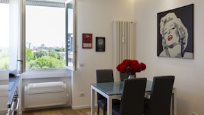 Un moderno comedor con mesa de vidrio, sillas negras y un jarrón con flores rojas. En la pared, un llamativo cuadro pop art de una mujer.