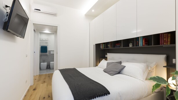 Un dormitorio moderno con una cama grande, un televisor de pantalla plana en la pared y una estantería con libros.