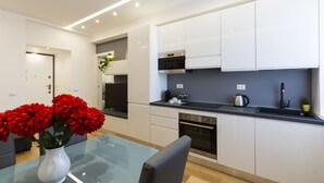 Una cocina moderna con armarios blancos, encimera negra y mesa de comedor de vidrio.