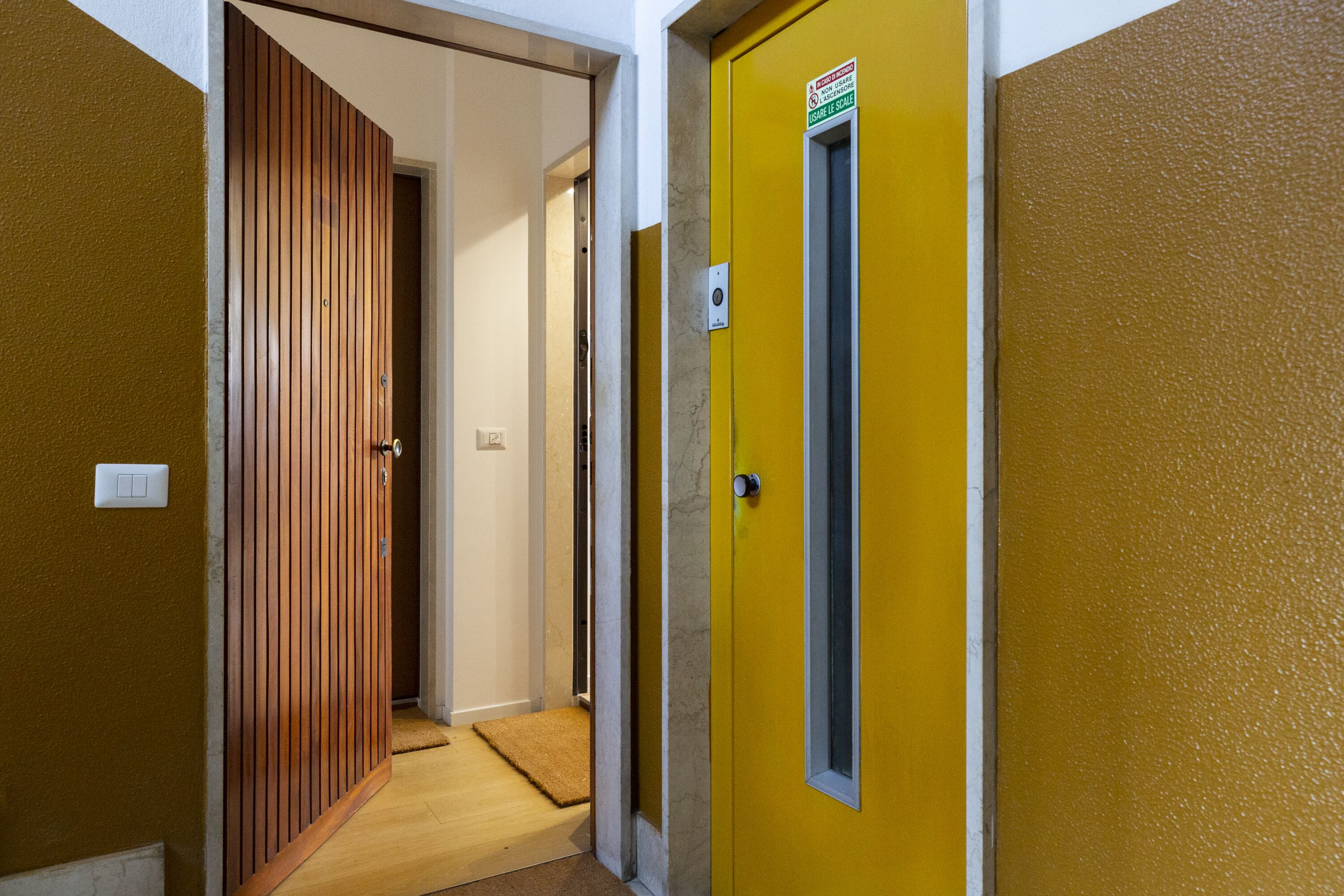 Un couloir avec une porte en bois et une porte jaune, les deux donnant sur des pièces.