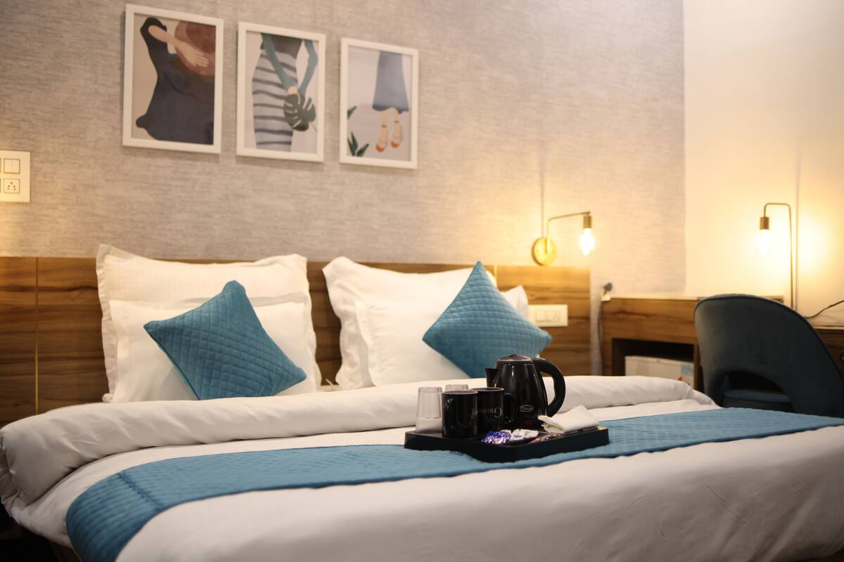A neatly made bed with blue and white bedding, a tray with a coffee pot and cups, and wall art above the bed.