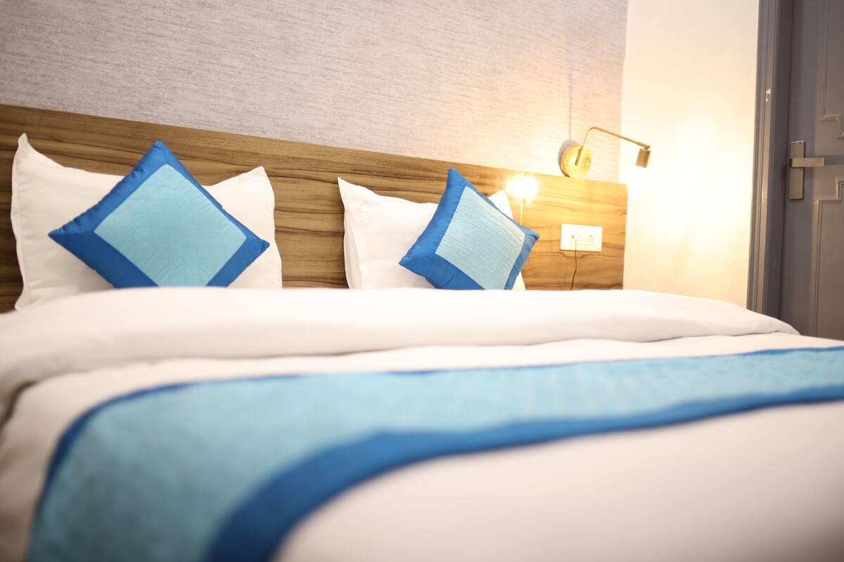 A neatly made bed with white and blue bedding, a wooden headboard, and a bedside lamp.