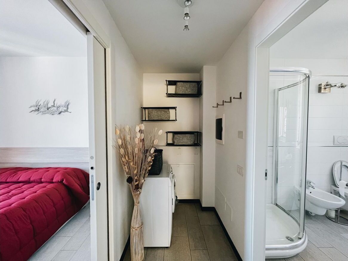 A compact hotel room with a bed, a washing machine, a shower, and a small kitchenette.