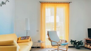 Un salon avec un canapé jaune, une petite table d’appoint en verre, un fauteuil, une plante en pot et un meuble pour la télévision.