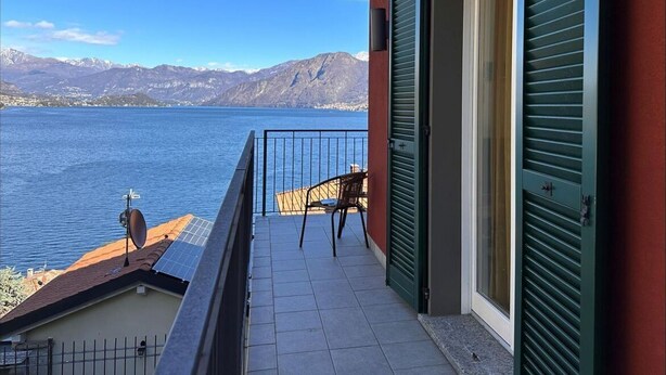 Un balcon donnant sur un lac et des montagnes, une chaise et une porte avec des volets.