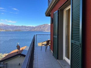 Een balkon met uitzicht op een meer en bergen, een stoel en een deur met luiken.