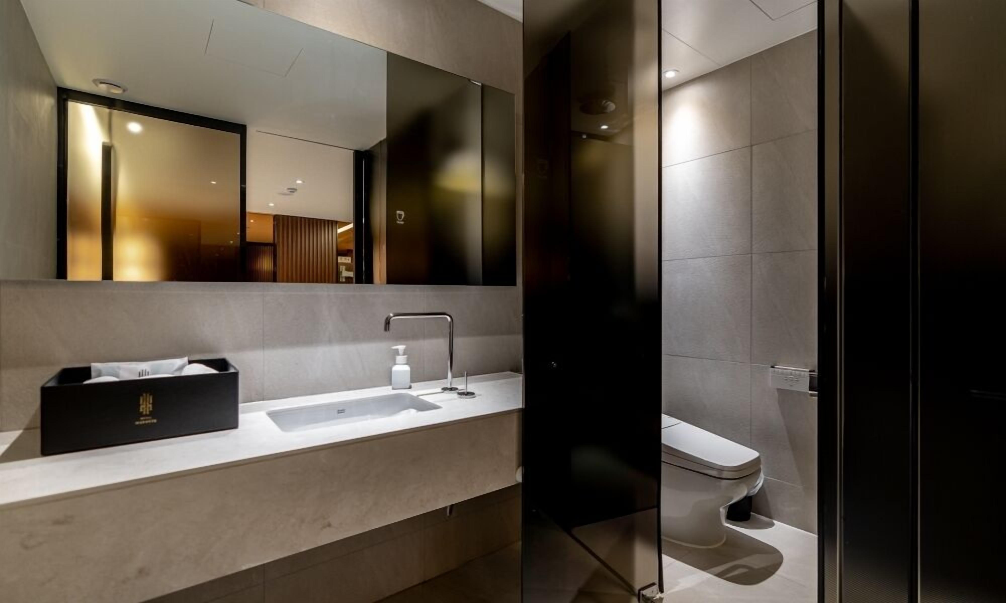 Un baño moderno con un espejo grande, un lavamanos blanco y un inodoro.