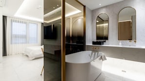 A modern hotel bathroom with a freestanding bathtub, a large mirror, and a vanity with a sink. - Uiwang Hotel Mayotte (Uiwang)