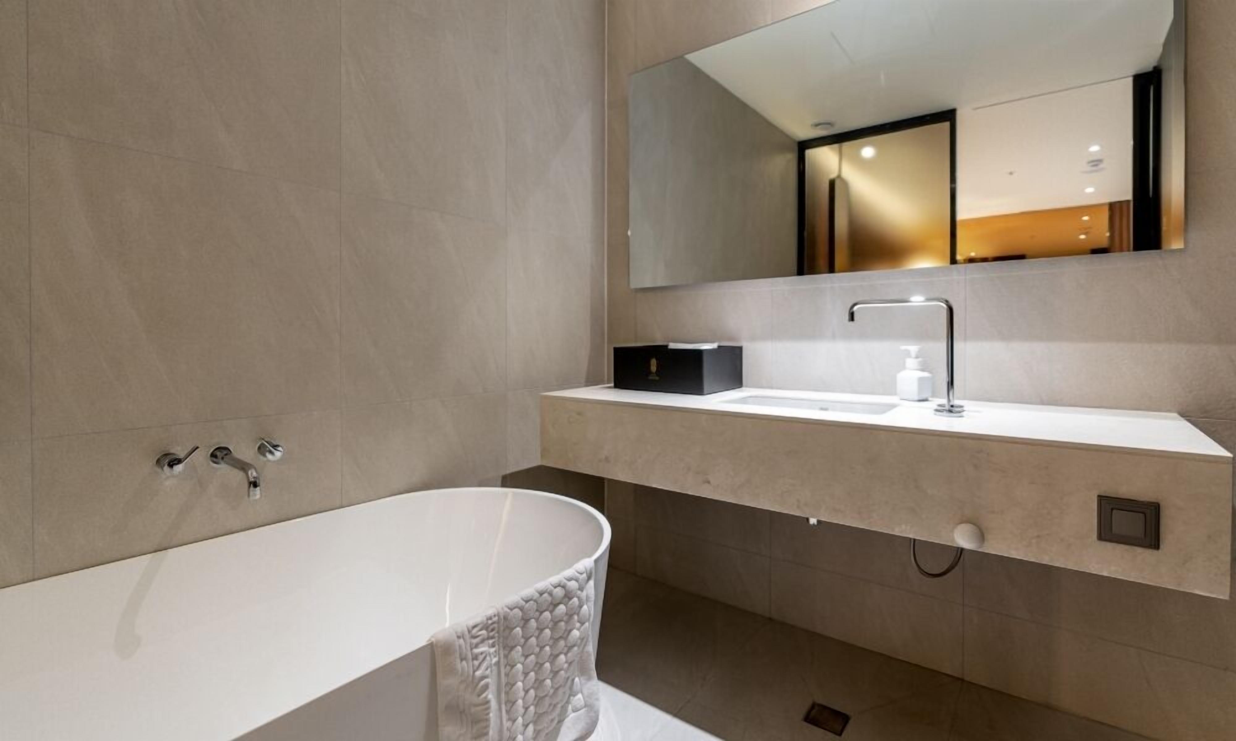 Un bany modern amb una banyera independent, un lavabo blanc amb mirall i una caixa negra al taulell.