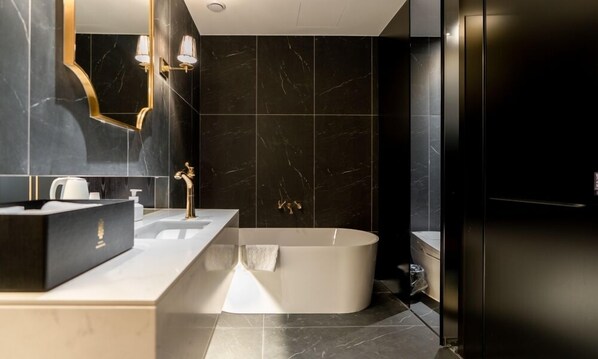 A modern bathroom with a freestanding bathtub, a vanity with a gold faucet, and dark marble tiles.
