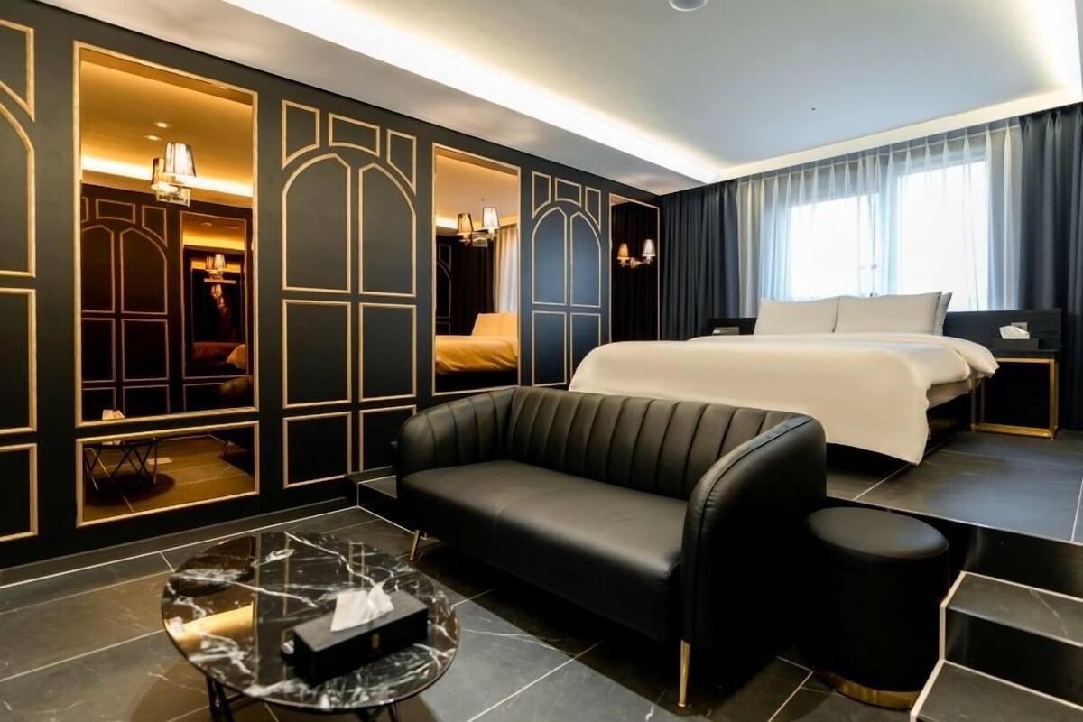 Un moderno cuarto de hotel con una cama grande, un sofá de cuero, una mesa de centro de mármol y vistas a la ciudad a través de amplias ventanas.