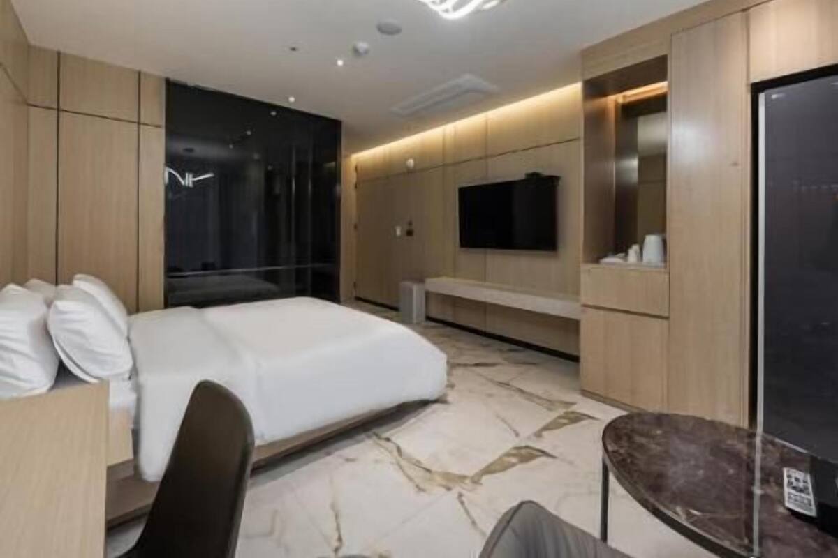 Una habitación de hotel moderna con una cama grande, un escritorio, una silla, un televisor montado en la pared y un minibar.
