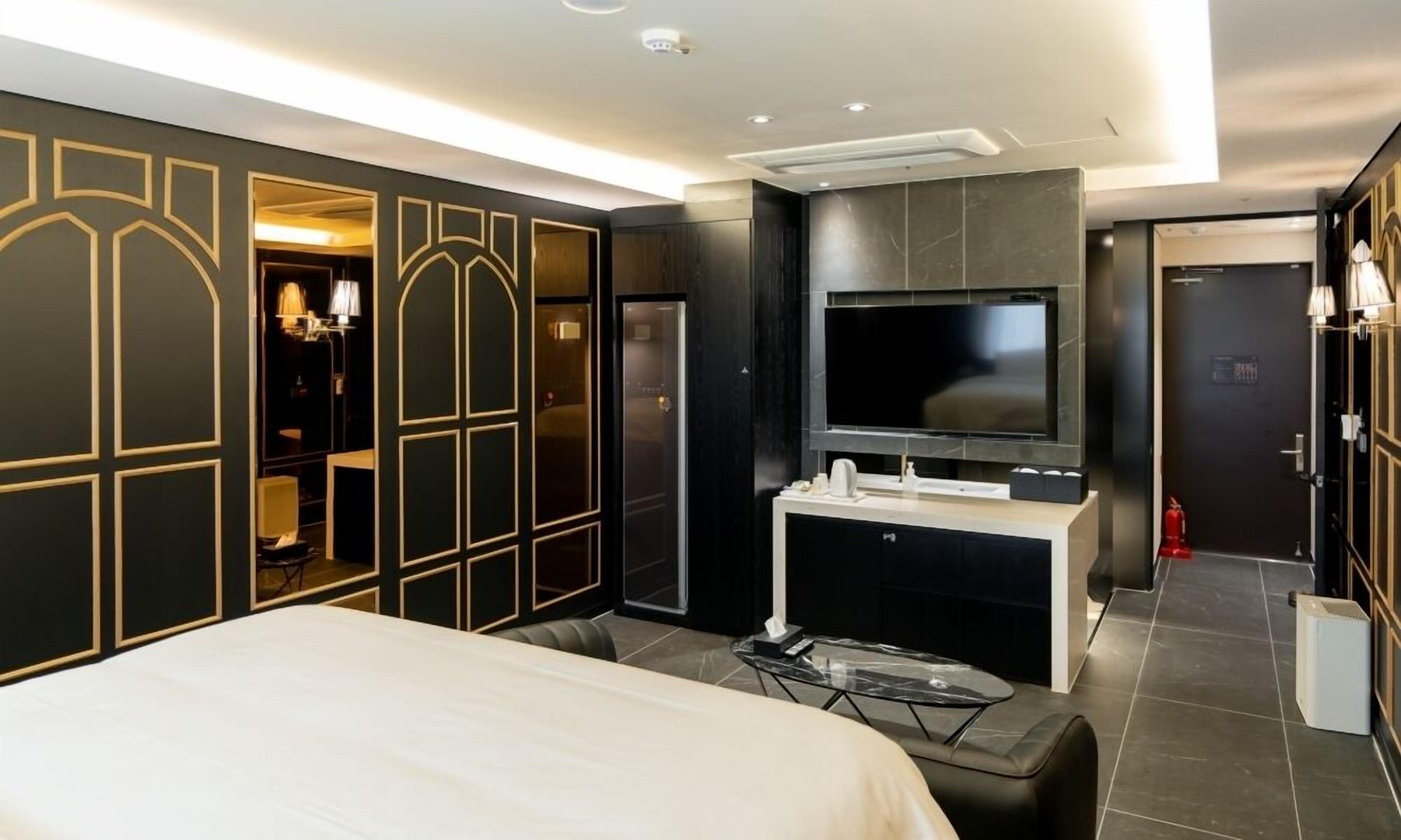 Una habitación de hotel moderna con una cama grande, un televisor montado en la pared, un tocador con espejo y un armario con espejo.
