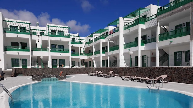 A swimming pool surrounded by white buildings with green balconies and a stone wall.