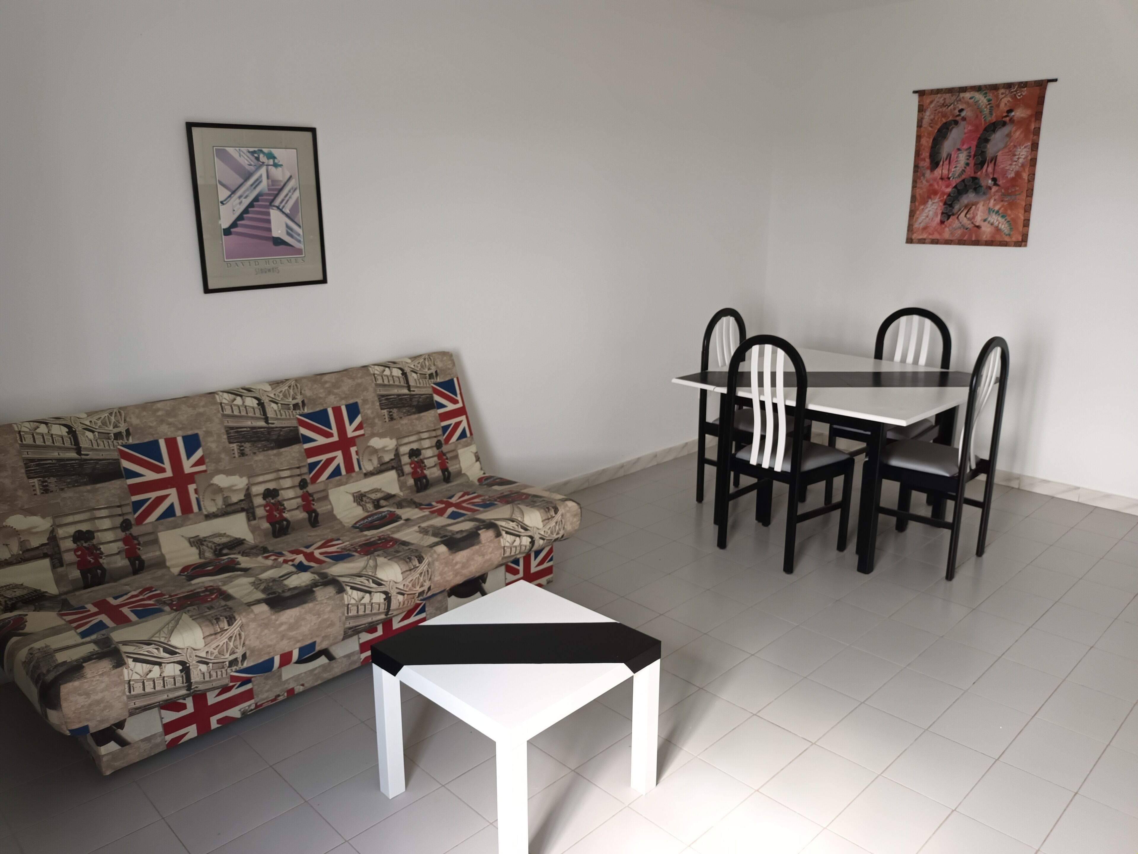 Una sala de estar con un sofá, una mesa de centro, una mesa de comedor con sillas y un cuadro en la pared.