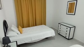 A bedroom with a bed, a bedside table with a lamp, a dresser, and a window with curtains.