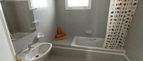 Une salle de bain avec un lavabo, un miroir, une fenêtre et un rideau de douche.