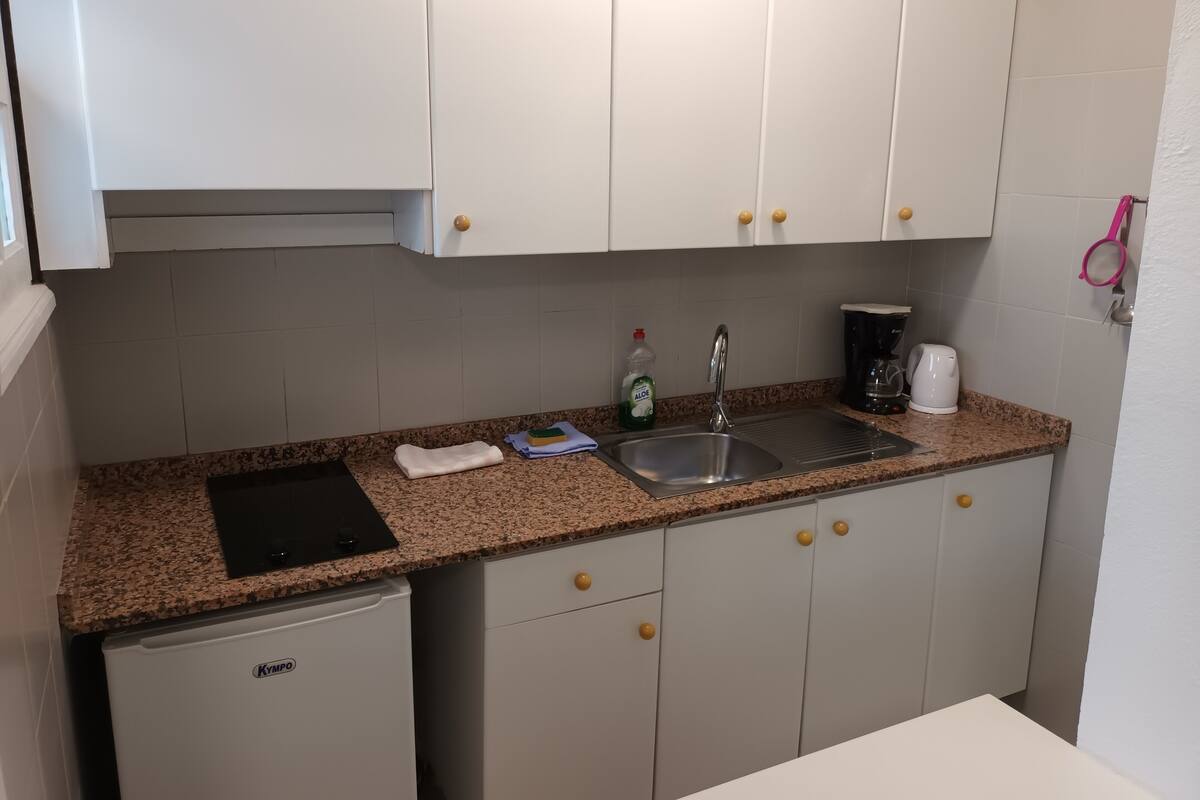 Une petite cuisine équipée de meubles blancs, d’un plan de travail en granit, d’un évier, d’une machine à café et d’un petit réfrigérateur.
