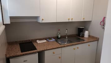 Una kitchenette con gabinetes blancos, encimera de granito, un lavamanos, cafetera y un refrigerador pequeño.