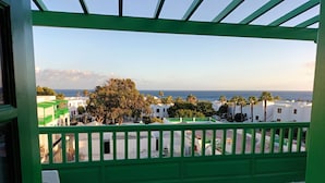 A balcony with a green railing overlooking a residential area with white buildings and palm trees.
