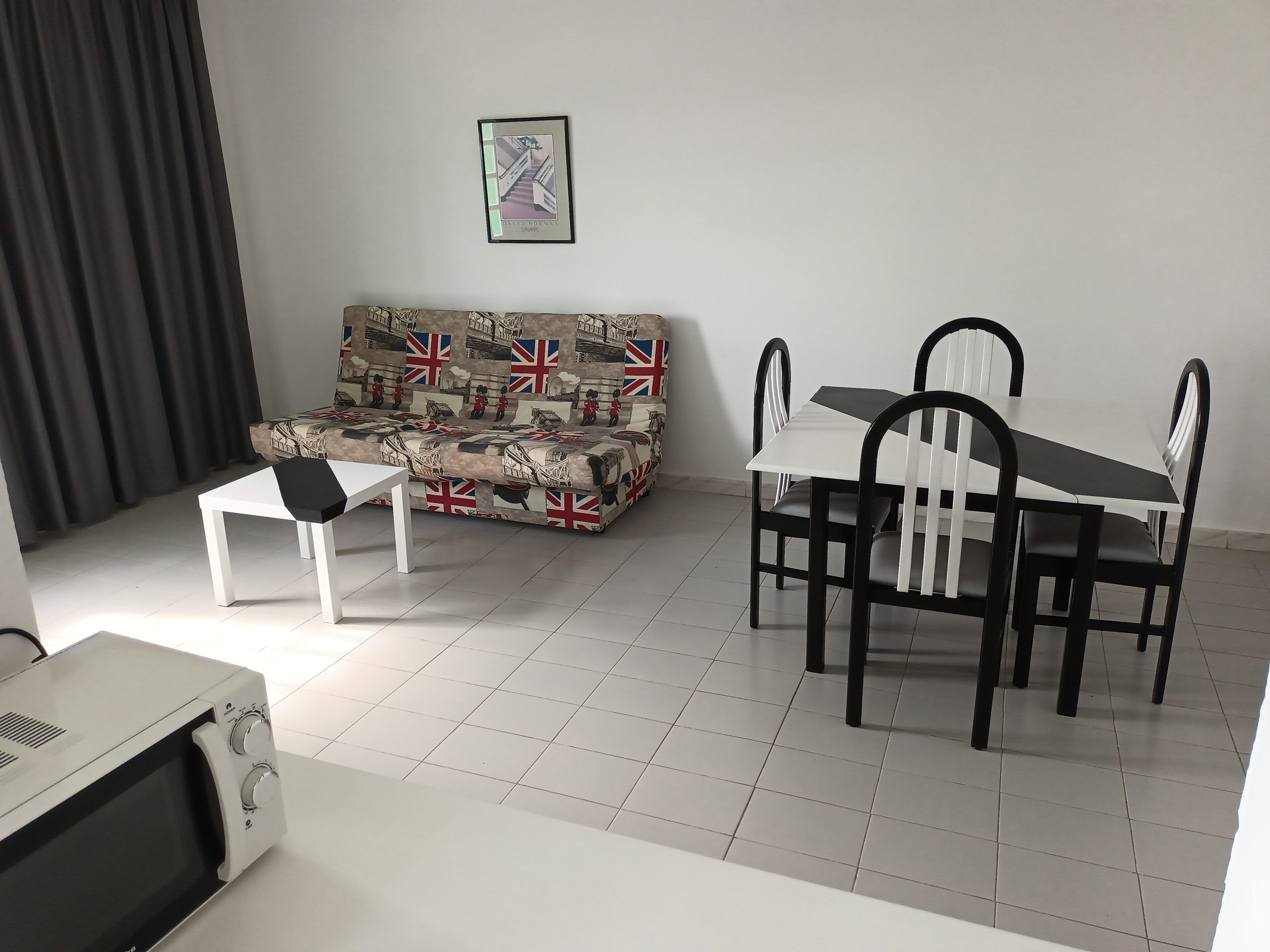 Ein Wohnzimmer mit einer Couch, einem Esstisch mit Stühlen, einem kleinen weißen Tisch und einer Mikrowelle.