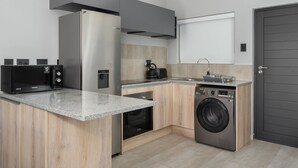 A compact kitchen with a built-in microwave, oven, and washing machine, a coffee maker, and a grey door.