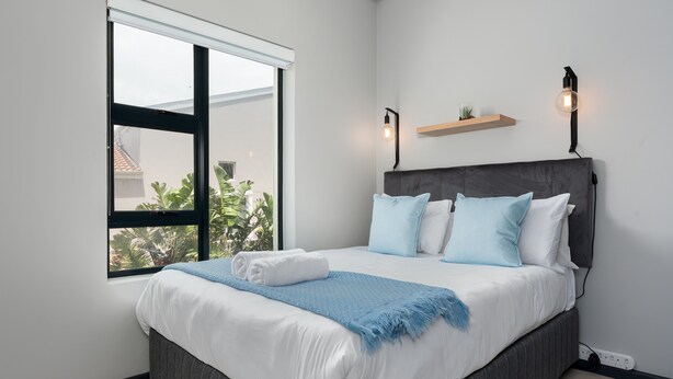 A modern bedroom with a large bed, a window, and a wall-mounted shelf.