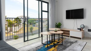 A modern living room with a large sliding glass door, a flat-screen TV, a wooden console table, and a colorful rug.