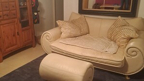 Un salon avec un canapé beige, un pouf assorti et un meuble en bois.