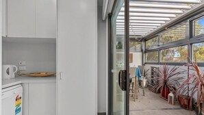 A modern kitchen with white cabinets, a dishwasher, and a glass door leading to a patio area with potted plants and a seating area.
