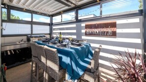 An outdoor dining area with wicker chairs and a table set for a meal, featuring a blue tablecloth and a wine bottle.