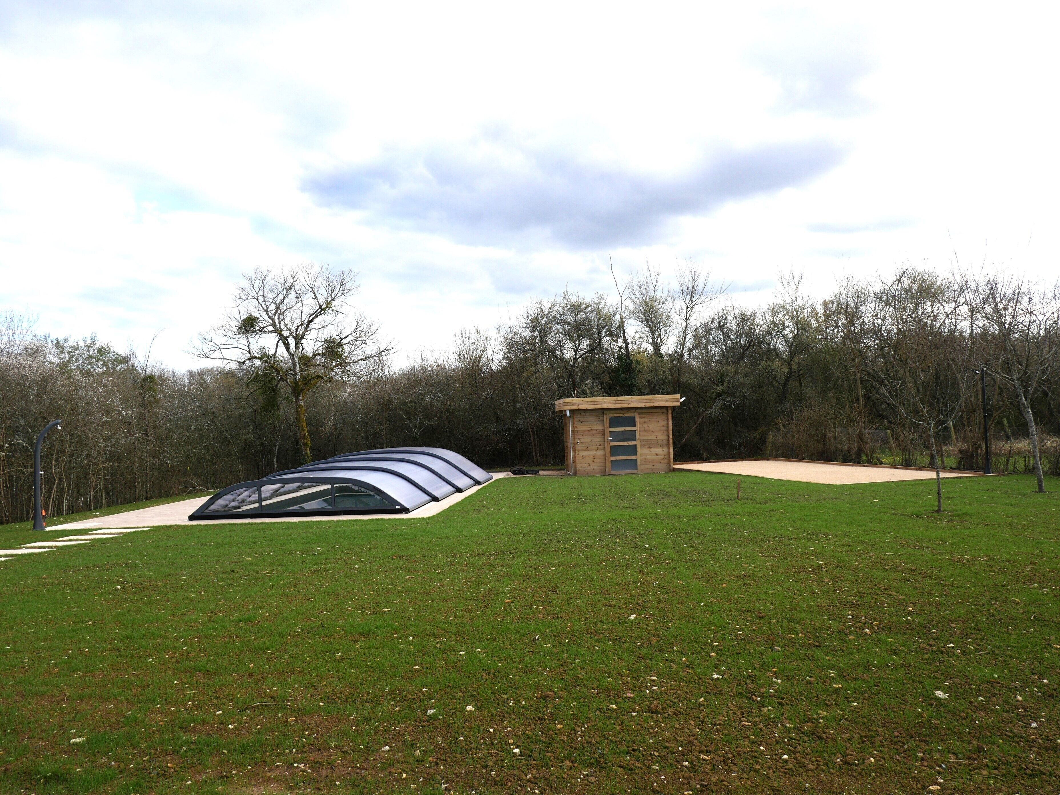 A grassy area with a small wooden structure and a transparent shelter.