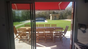 A patio area with a table and chairs, a red awning, and a view of a backyard with a pool and a car. - LA ROTIERE LODGE DU CERVOLET 4-bedroom house in the Loire Valley (Fontaines-en-Sologne)