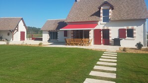 A two-story house with a red awning, a covered patio with wooden furniture, and a well-maintained lawn. - LA ROTIERE LODGE DU CERVOLET 4-bedroom house in the Loire Valley (Fontaines-en-Sologne)
