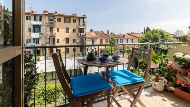 A balcony with two blue cushioned chairs, a small round table with a kettle, and potted plants. - Relax in vibrant San Frediano (Firenze)
