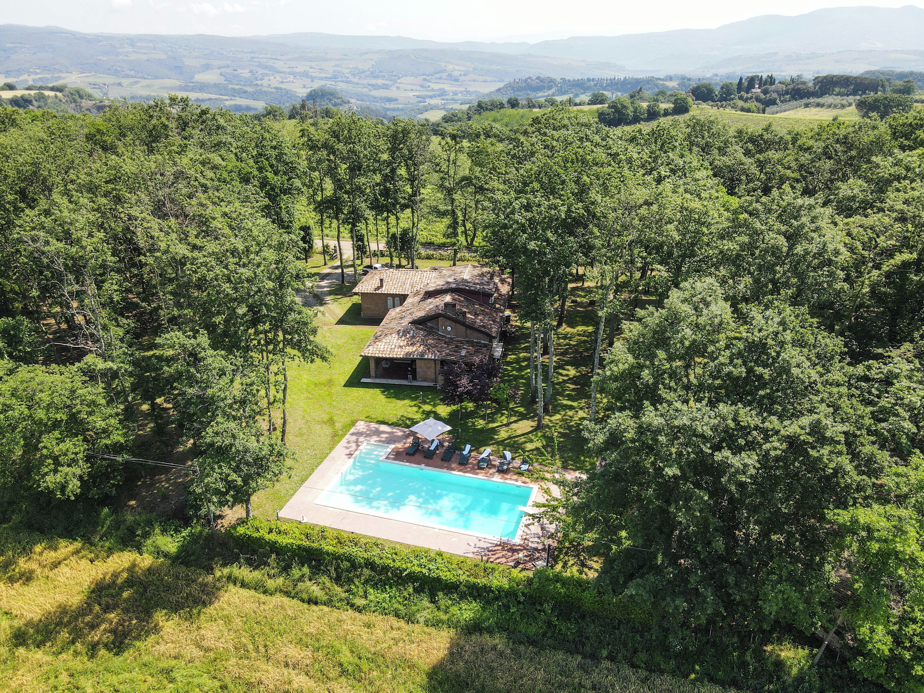 A house surrounded by dense forest with a swimming pool and a thatched-roof structure.